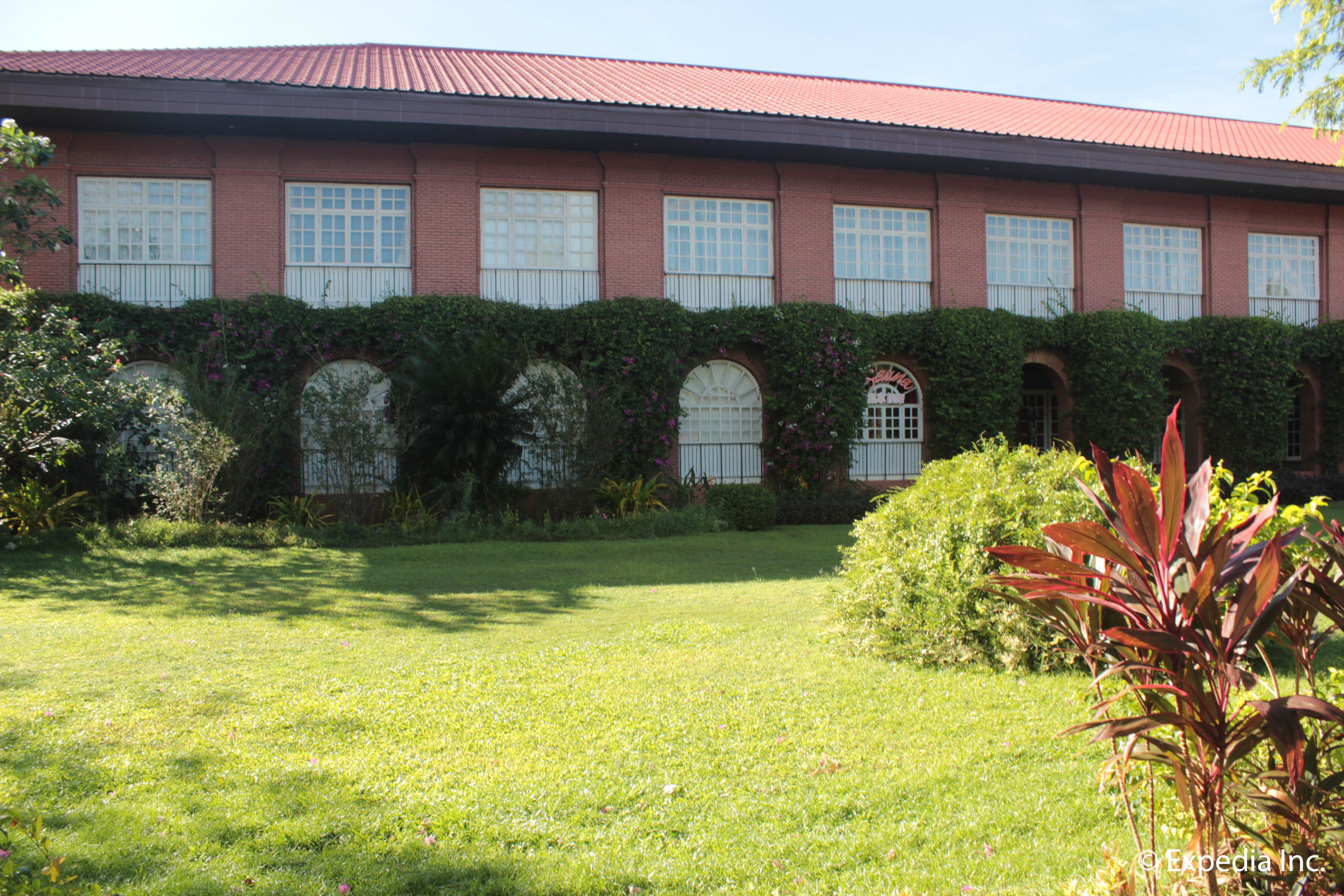 A building with a red roof, multiple windows, and a well-maintained garden with grass and shrubs.
