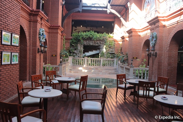 An indoor courtyard with brick walls, a stone staircase, and multiple tables and chairs. - Fort Ilocandia Resort Hotel (Laoag)
