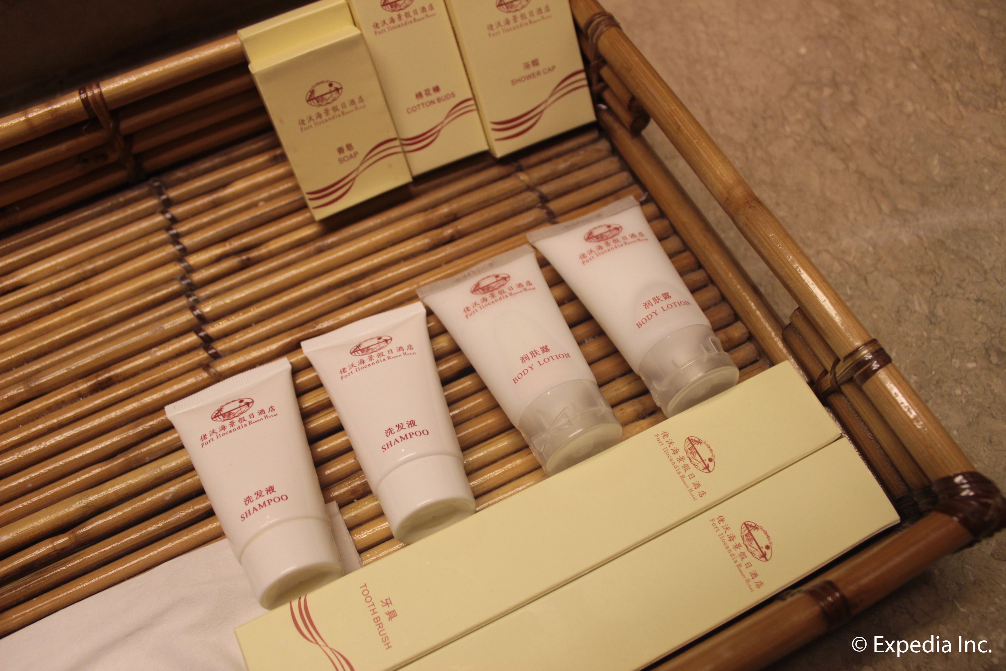 A set of toiletries arranged on a bamboo mat, including shampoo, body lotion, and cotton buds.