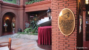 A brick building with a red table and chairs outside, a sign for 'Piano Lounge', and a staircase leading to an upper level. - Fort Ilocandia Resort Hotel (Laoag)