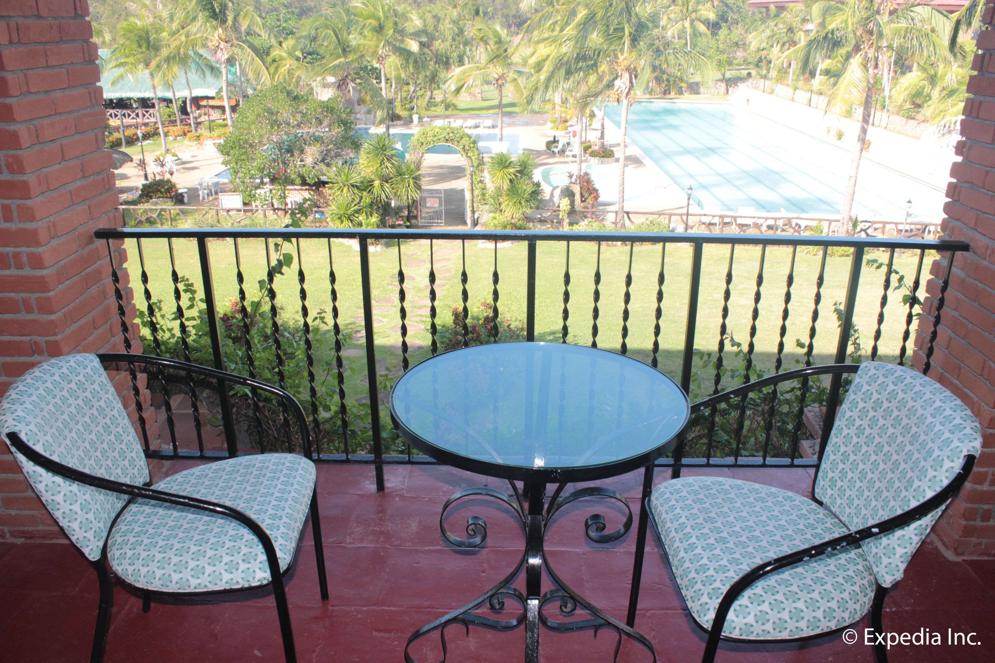 Un balcón con dos sillas y una mesa, con vistas a una piscina y palmeras.