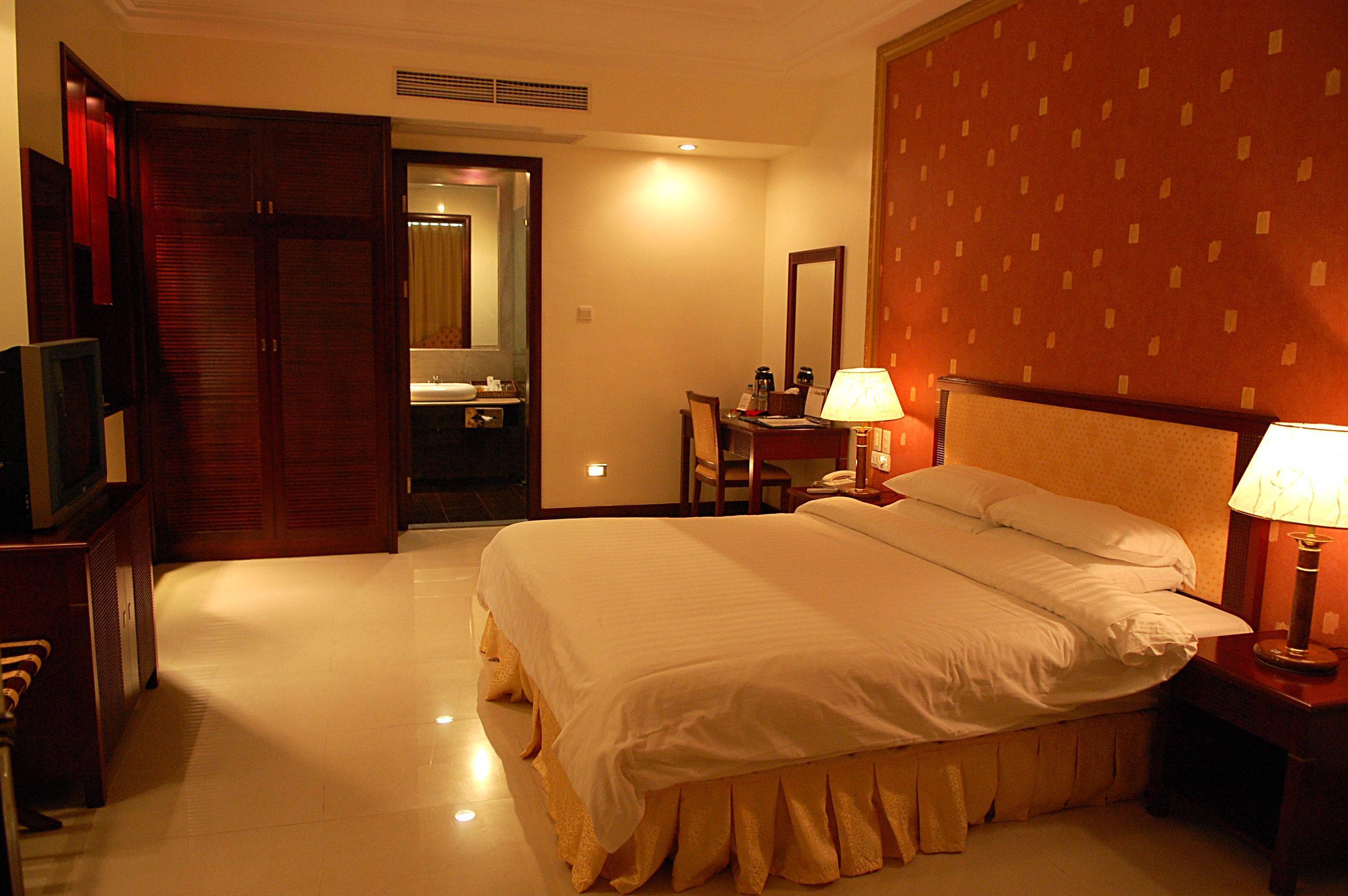 A hotel room with a large bed, bedside lamps, a desk with a chair, a television, and a wardrobe.