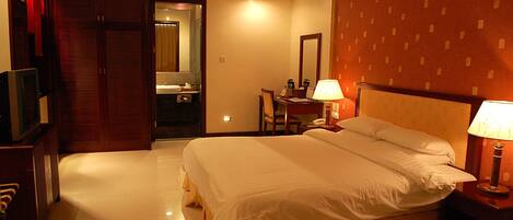 A hotel room with a large bed, bedside lamps, a desk with a chair, a television, and a wardrobe.