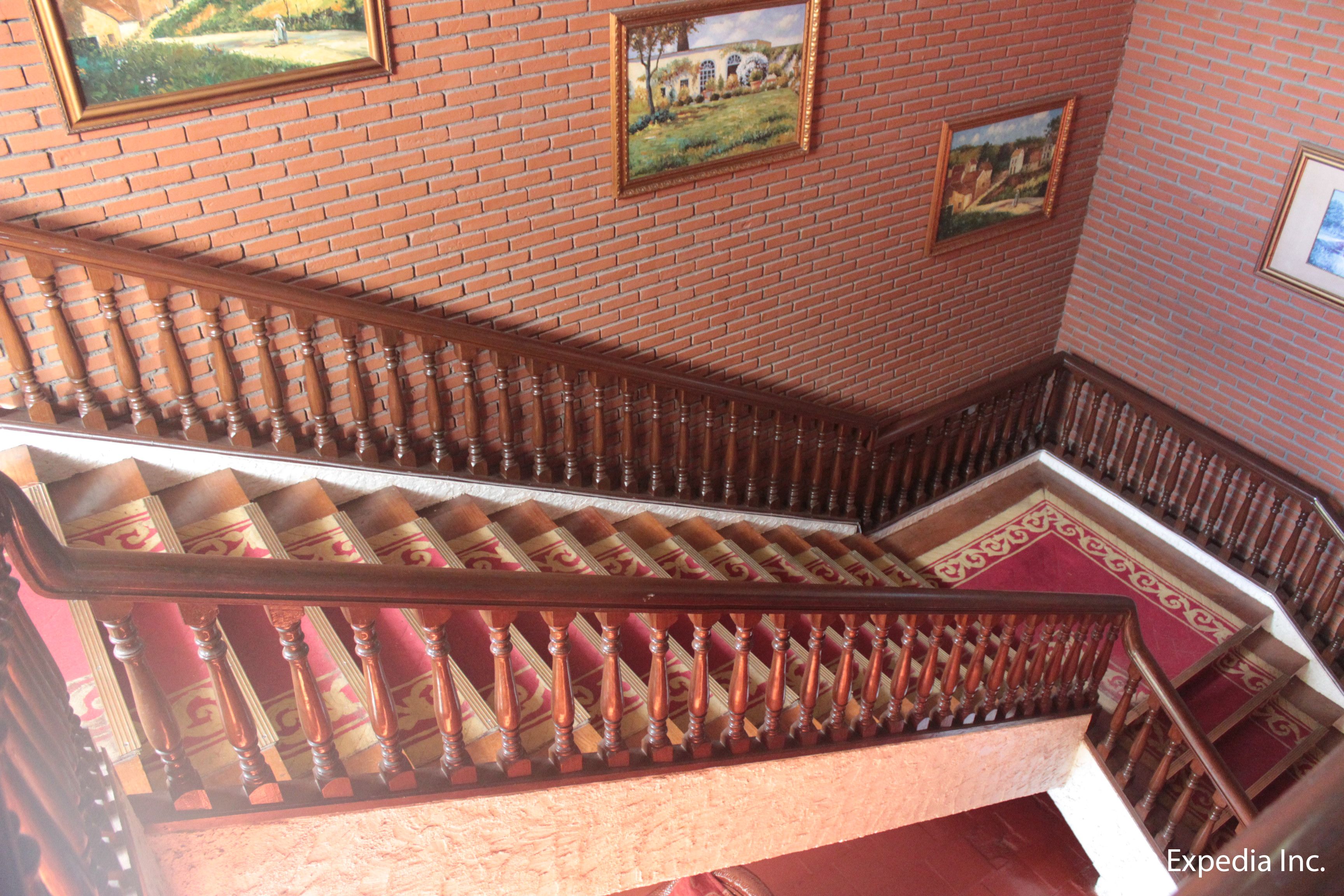 A wooden staircase with a red carpet, brick walls, and framed pictures.
