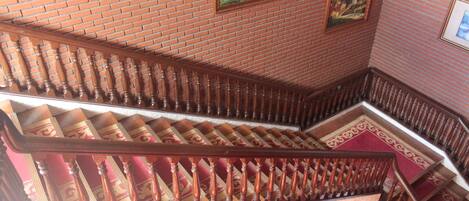 A wooden staircase with a red carpet, brick walls, and framed pictures.
