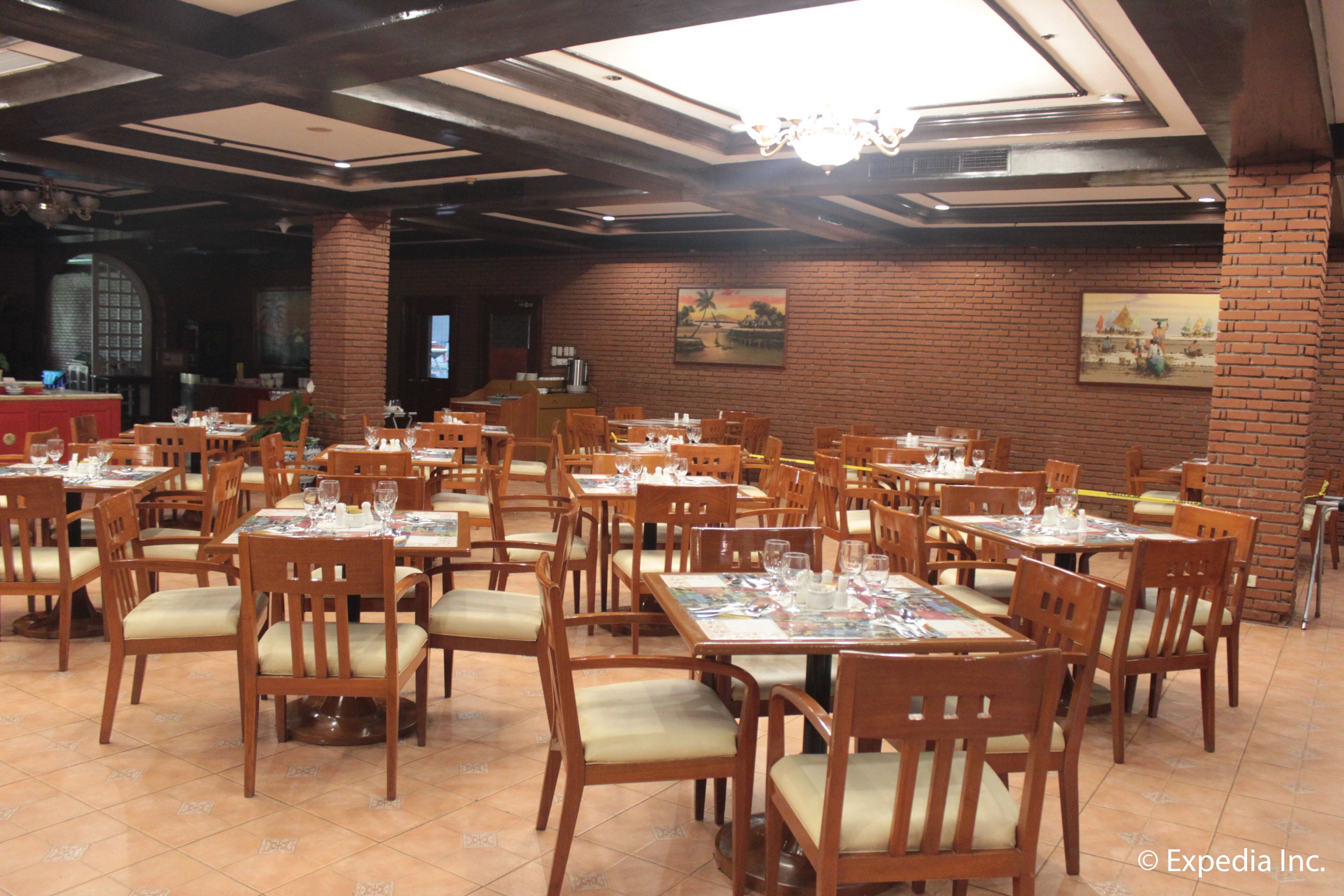 Een restaurant met meerdere houten tafels en stoelen, bakstenen muren en een kroonluchter.