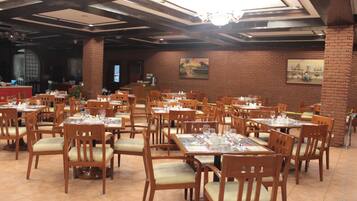 A restaurant with multiple wooden tables and chairs, brick walls, and a chandelier.
