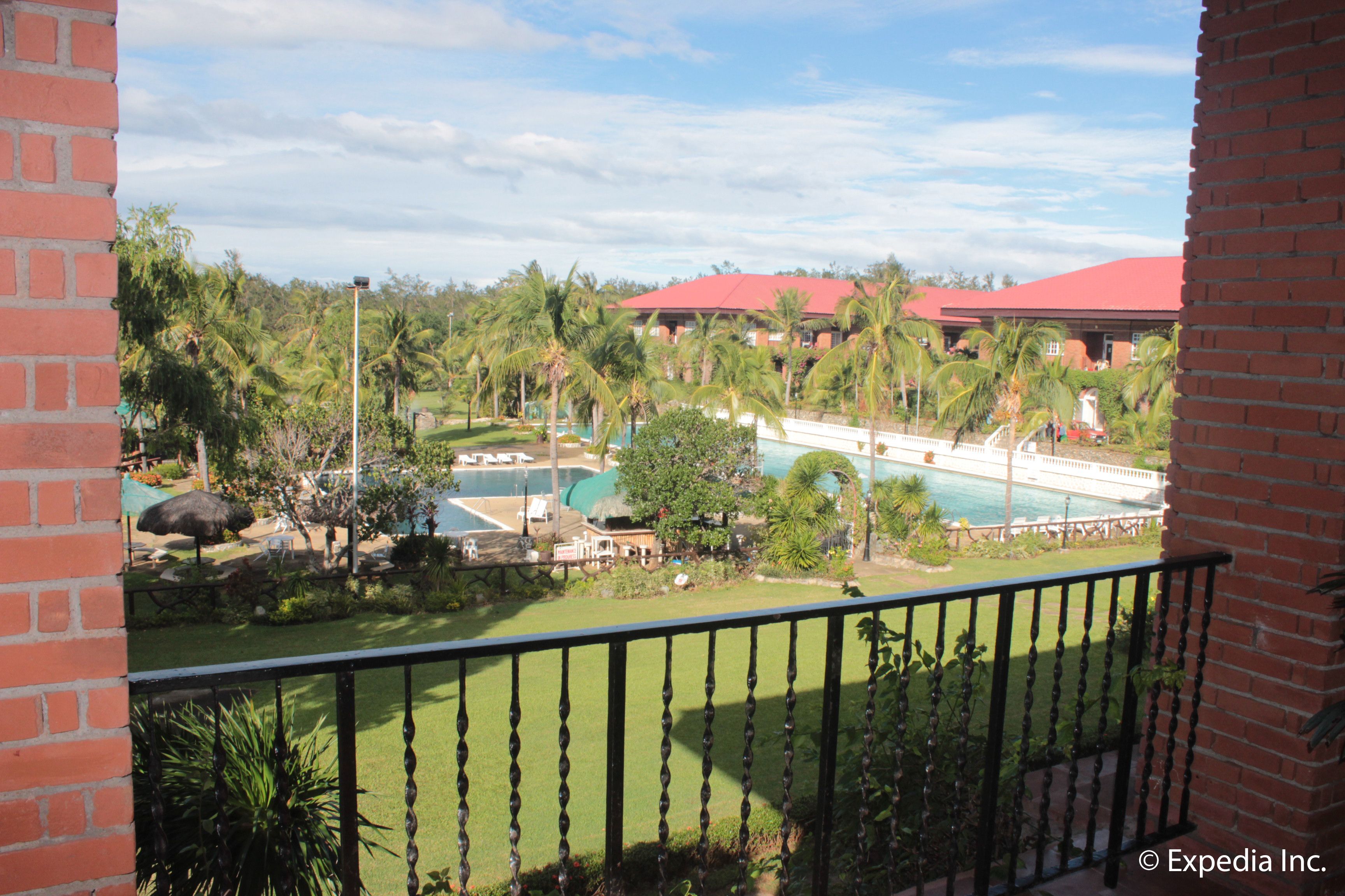 A view of a hotel with a pool, palm trees, and a red-roofed building.
