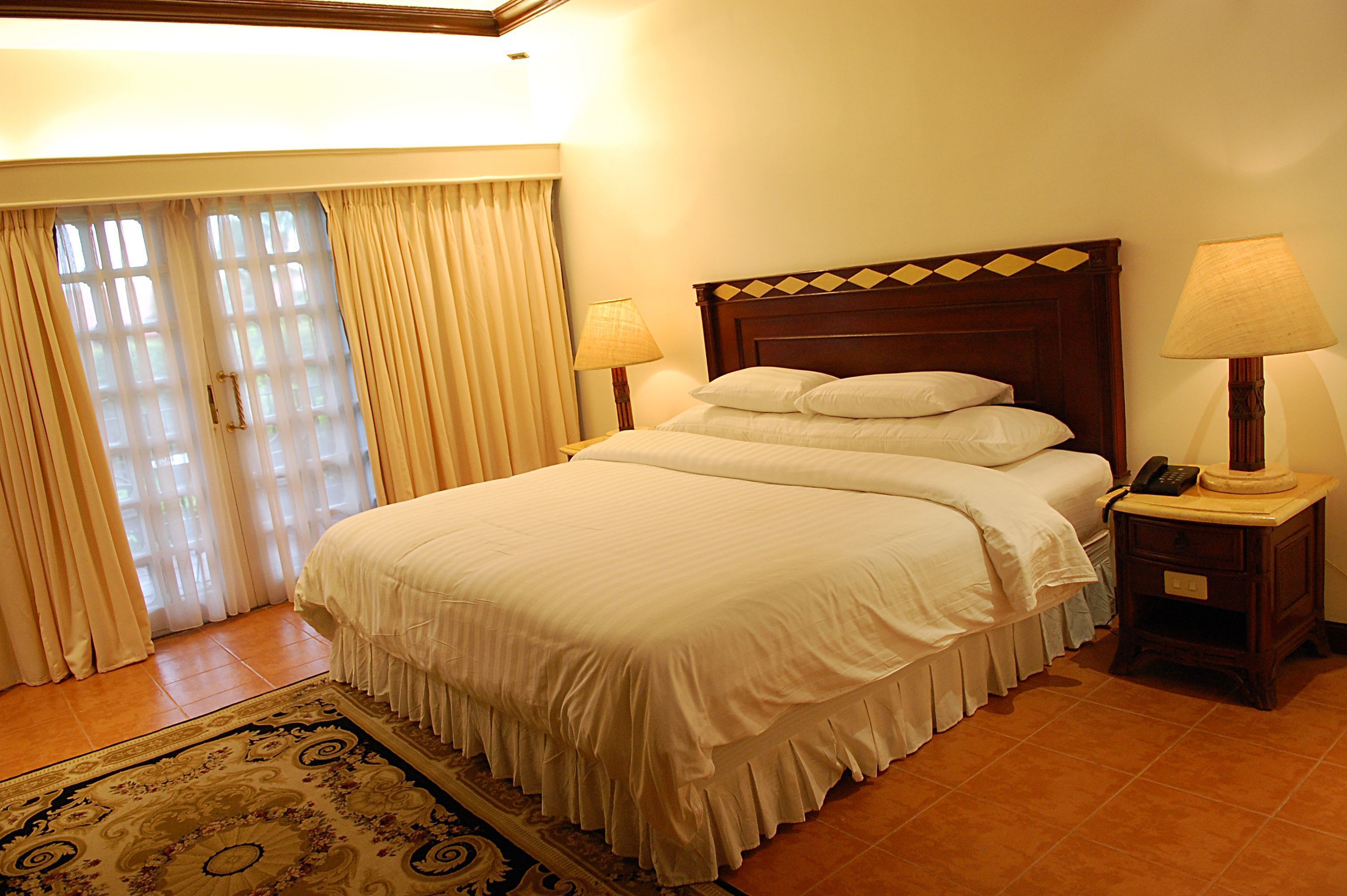 A neatly made bed with white linens, a wooden headboard, and two bedside lamps.