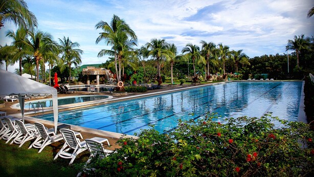 A swimming pool with lounge chairs and palm trees. - Fort Ilocandia Resort Hotel (Laoag)