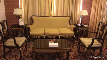 A hotel room with a sofa set, two armchairs, a coffee table, and two lamps.