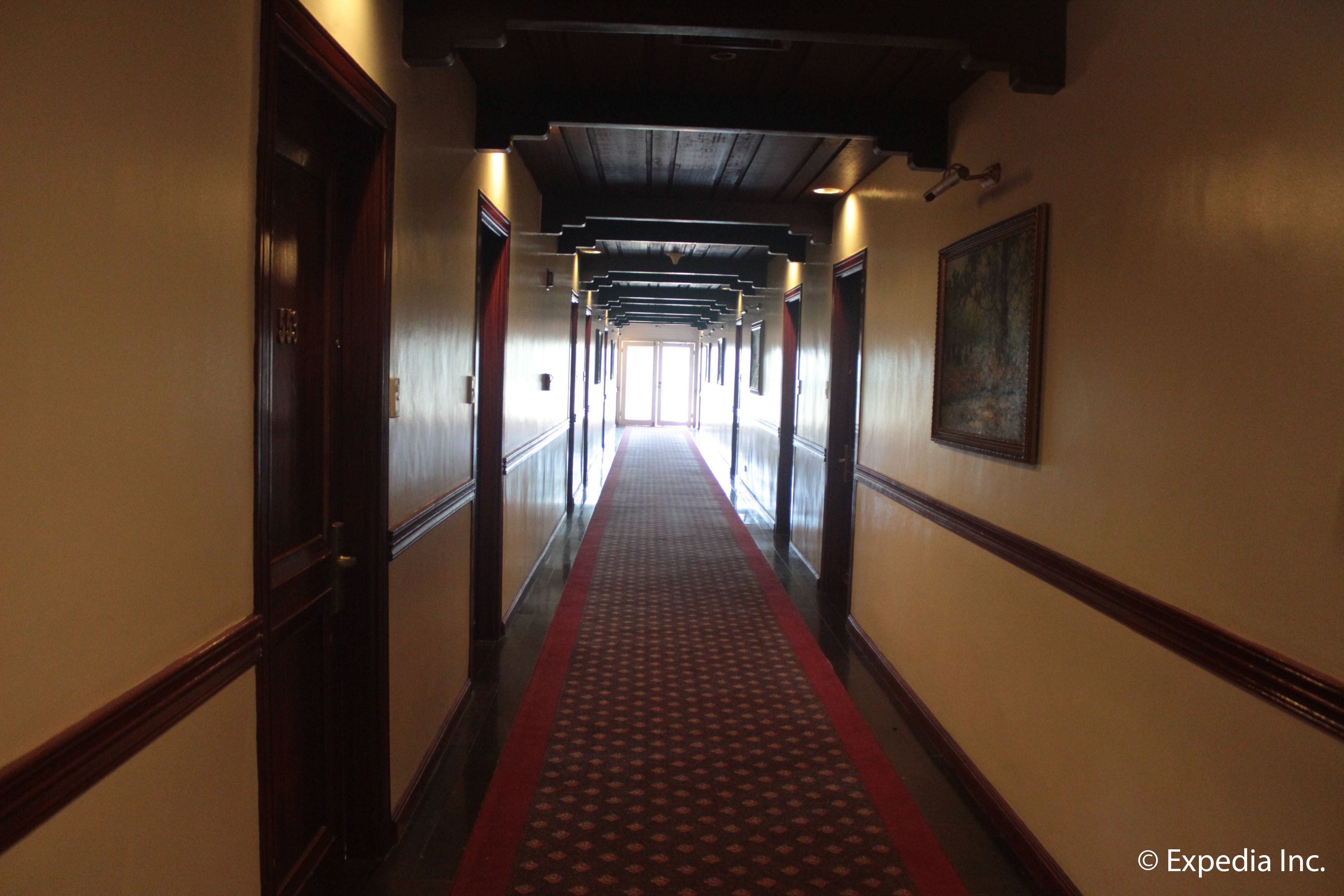 A long hallway with a red carpet, wooden doors, and a painting on the wall.