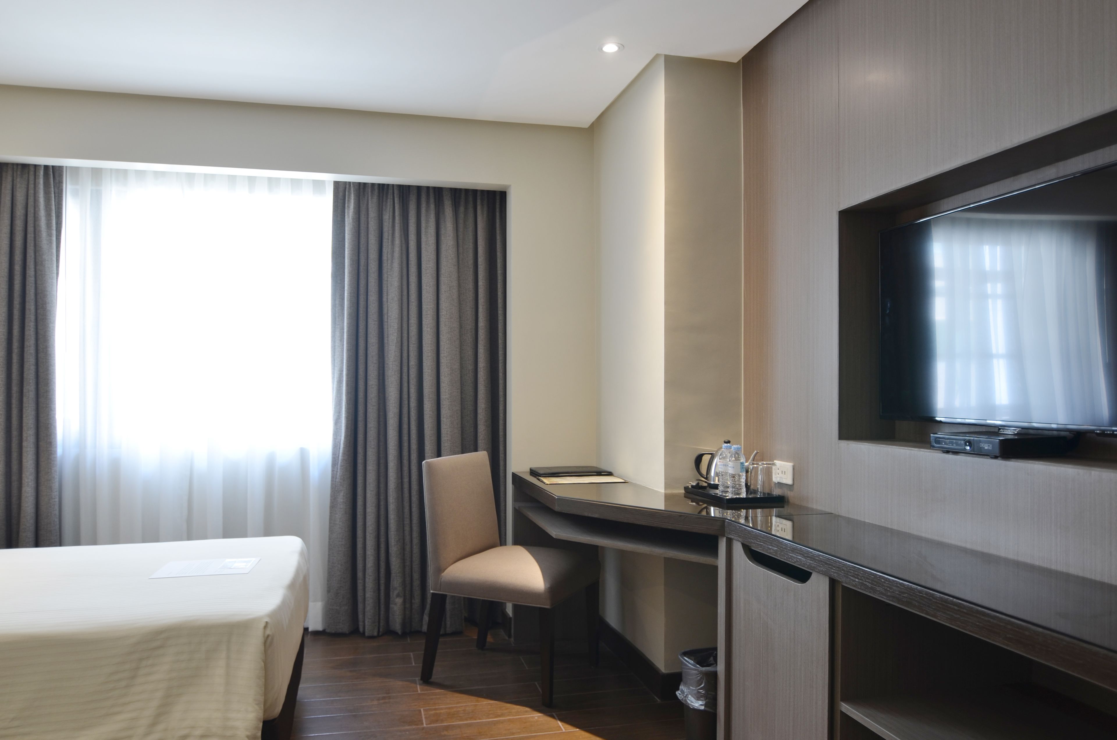 A hotel room with a bed, a desk, a chair, a TV, and a window with curtains.