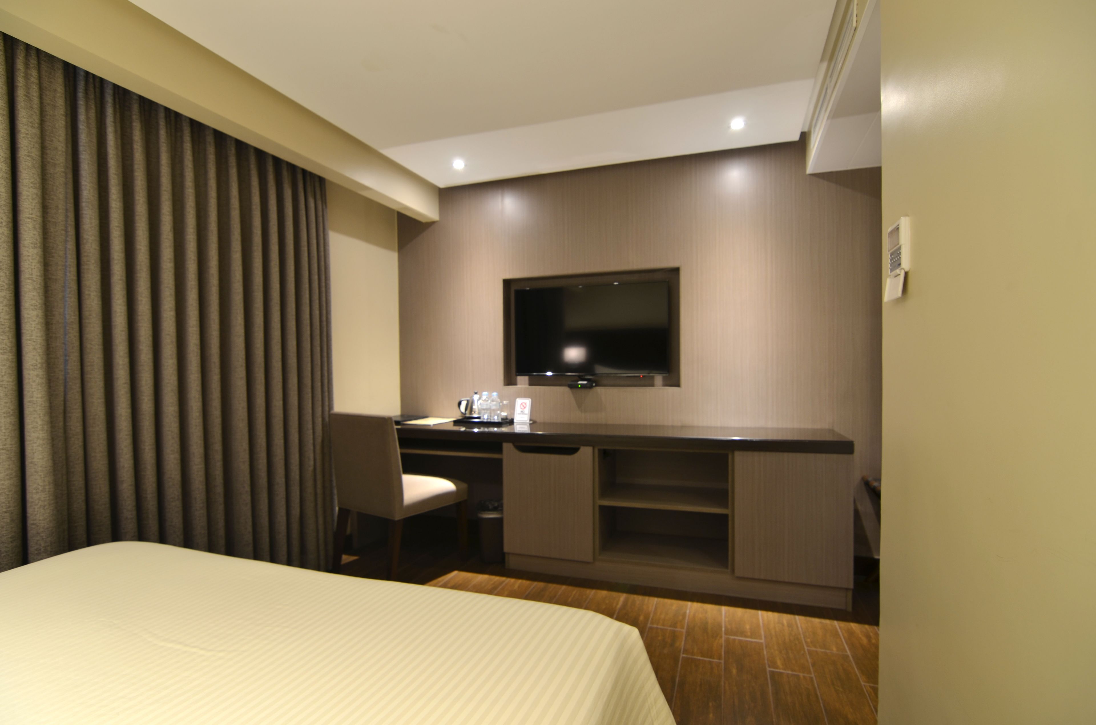 A hotel room with a bed, a desk with a flat-screen TV, a chair, and a small kitchenette area.