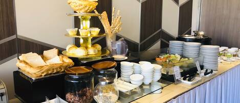 A buffet setup with various food items including bread, pastries, and condiments.