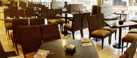 Un restaurante con varias mesas y sillas, ventanas amplias y vista a la calle.
