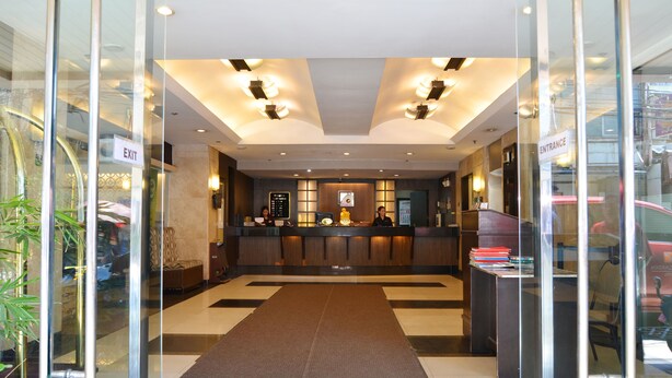 A hotel reception area with a reception desk, a large brown rug, and a glass wall on the left. - Pearl Garden Hotel (Manila)