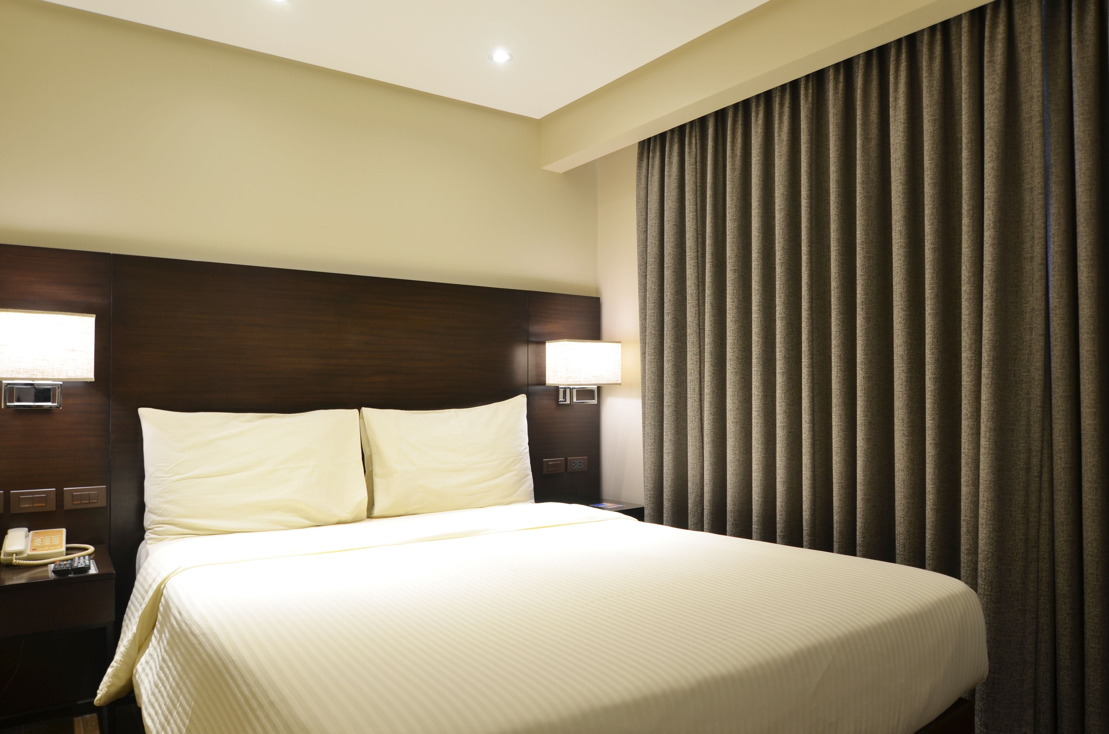 A hotel room with a large bed, two bedside lamps, a nightstand with a phone, and a curtain.