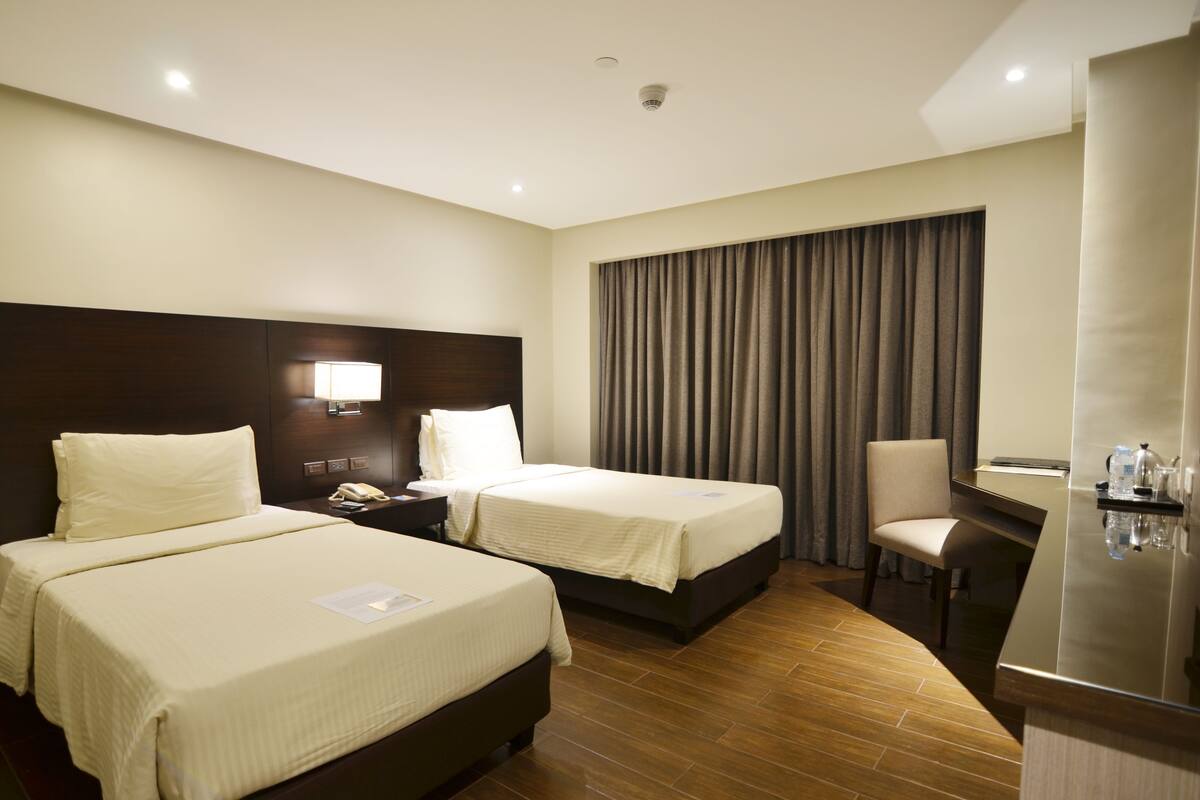 A hotel room with two beds, a desk, a chair, a nightstand, and a large window with curtains.