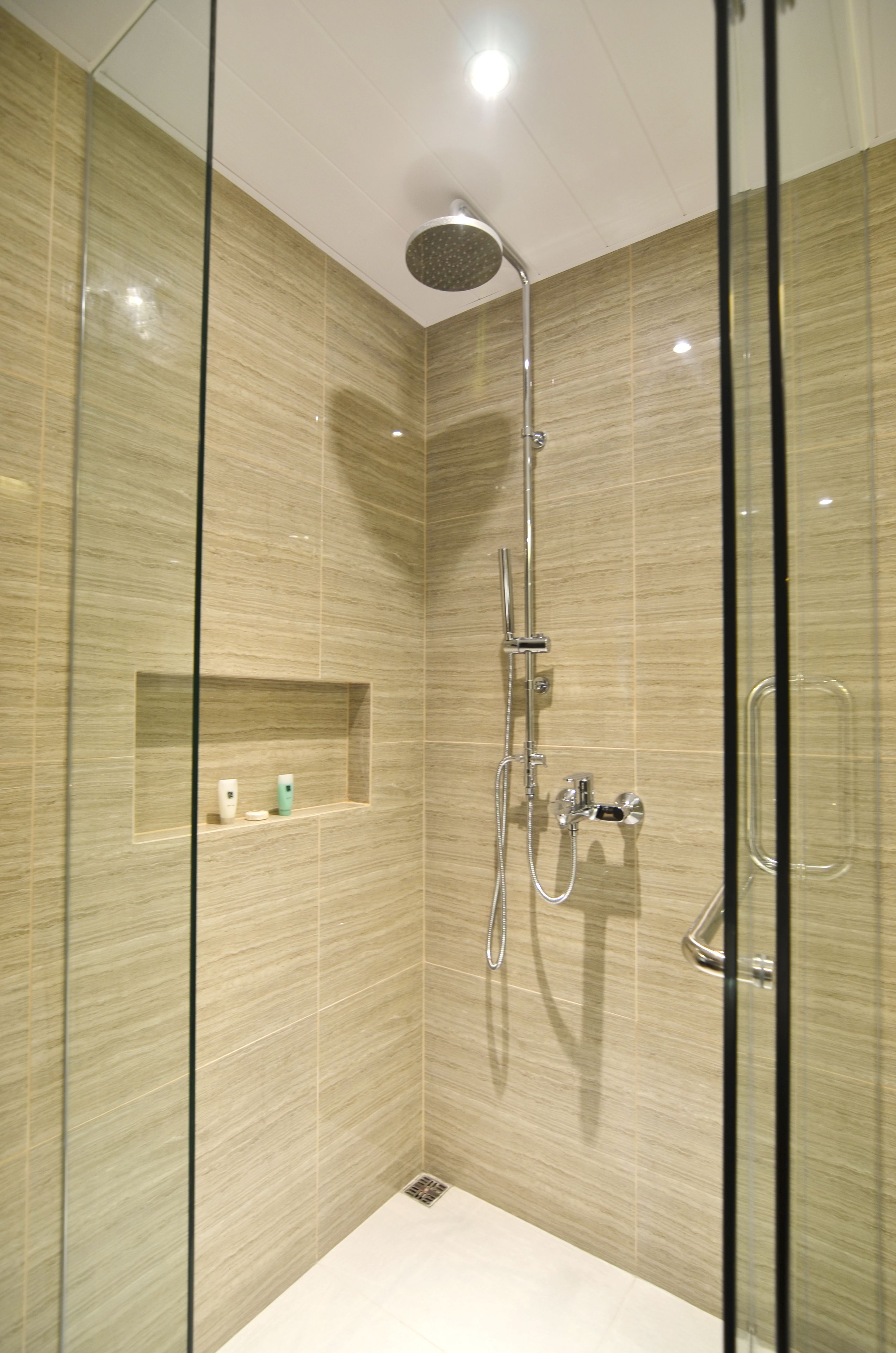 A modern shower with a glass enclosure, a built-in shelf with toiletries, and a handheld showerhead.