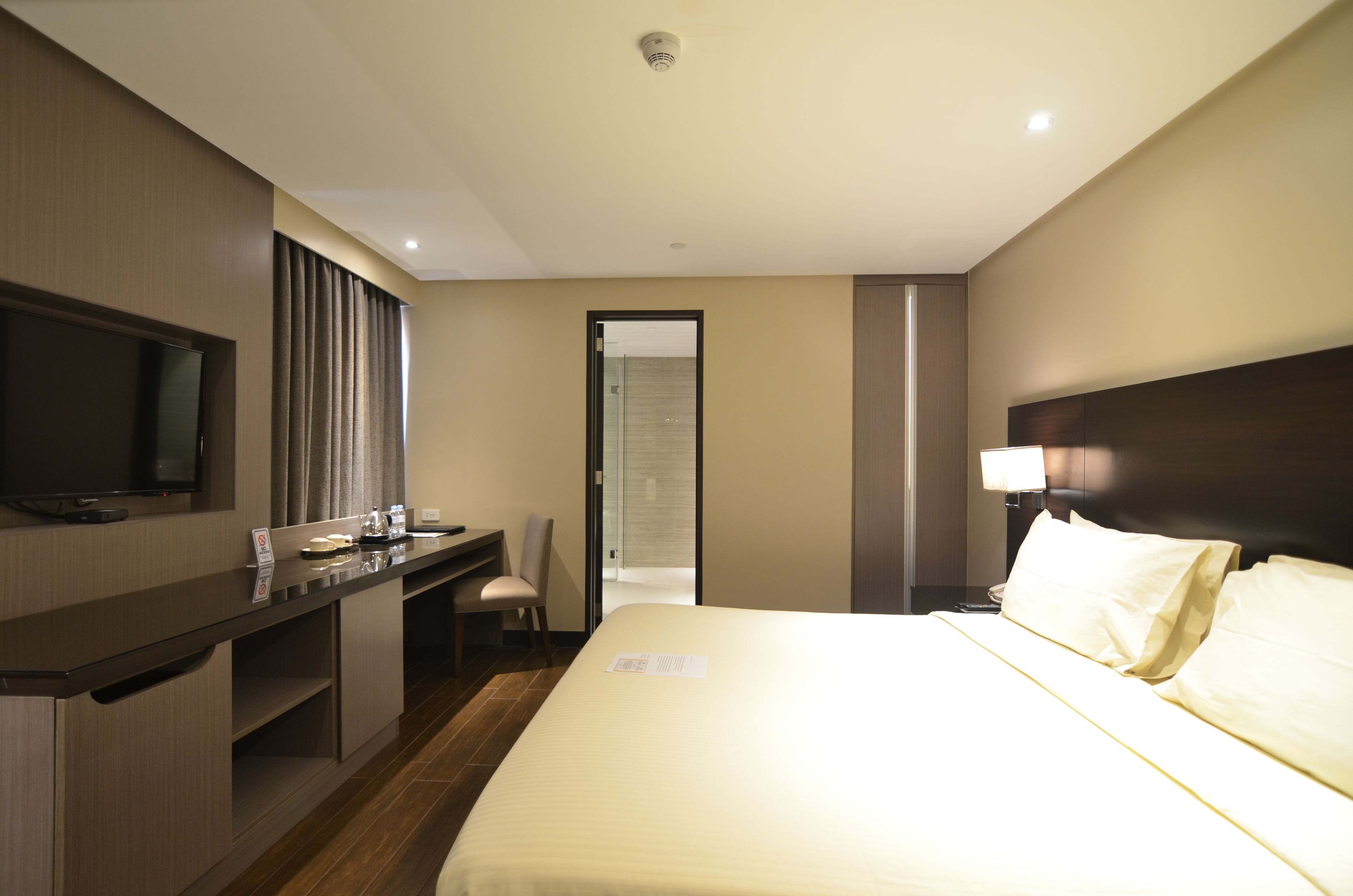 A hotel room with a bed, a desk, a chair, a television, and a door leading to another room.