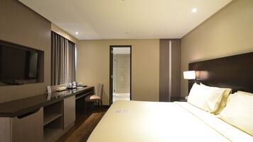 A hotel room with a bed, a desk, a chair, a television, and a door leading to another room.