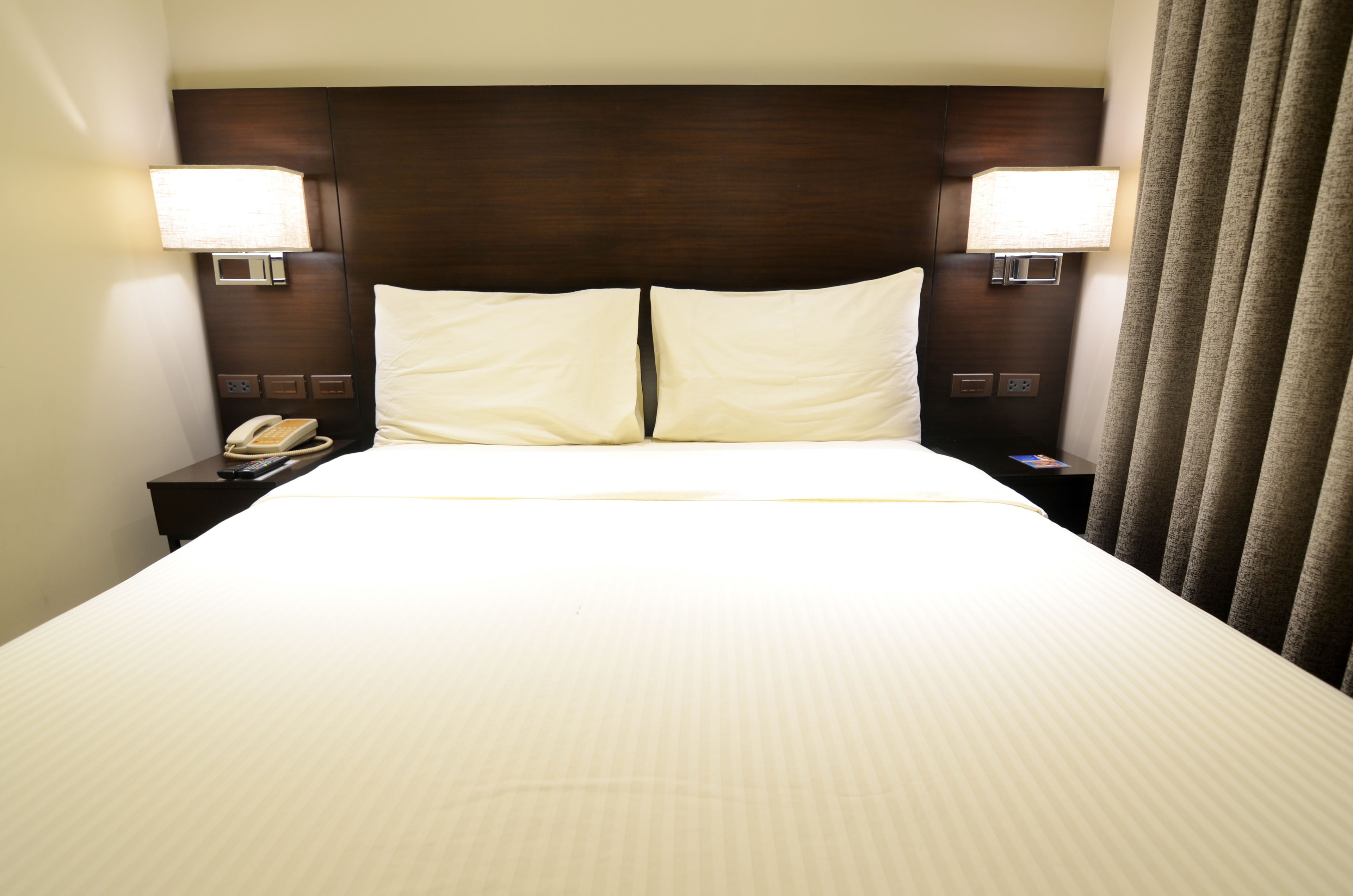 Habitación de hotel con una cama grande, dos lámparas de noche, una mesita de noche con teléfono y una cortina.