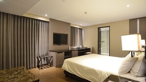 A hotel room with a bed, desk, chair, TV, and a bathroom visible through a glass door. - Pearl Garden Hotel (Manila)
