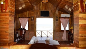 A cozy cabin room with wooden walls, a television, and a large window with curtains. - Vinh Suong Seaside (Mui Ne)