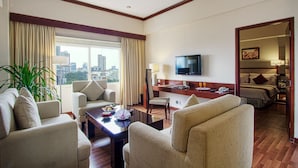 Quarto de hotel com vista para a cidade, televisão de tela plana, mesa de jantar e área de estar confortável.