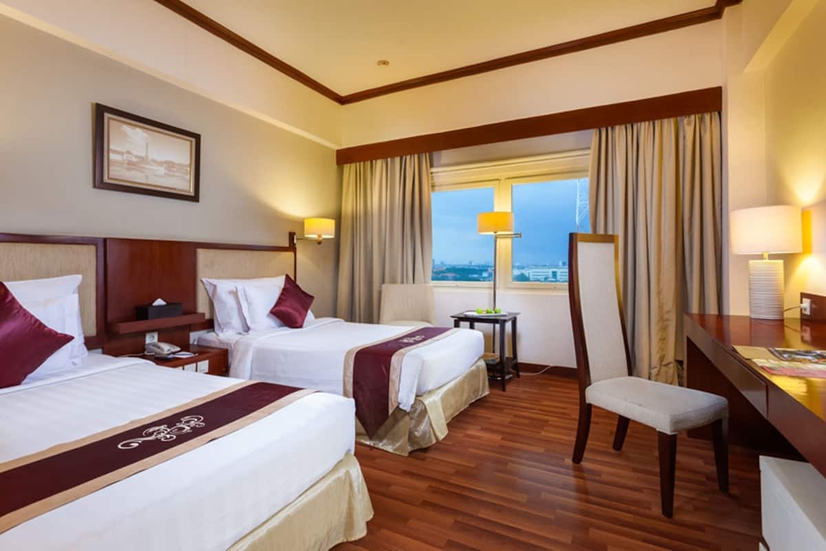 A hotel room with two beds, a desk, a chair, and a window with curtains.
