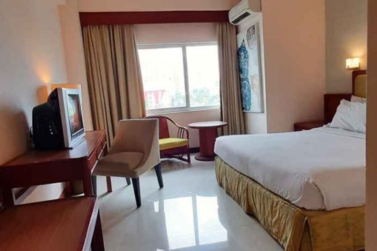 A hotel room with a bed, a desk, a chair, a small table, and a window with curtains.