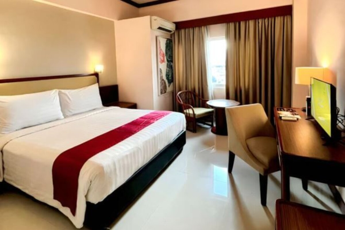 A hotel room with a bed, a desk, a chair, and a small table.
