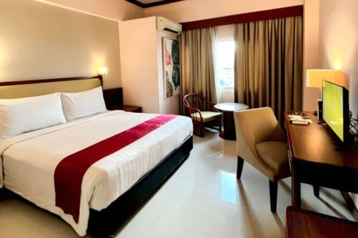 A hotel room with a bed, a desk, a chair, and a small table.