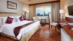 Quarto de hotel com uma cama grande, uma escrivaninha, uma cadeira e uma televisão.