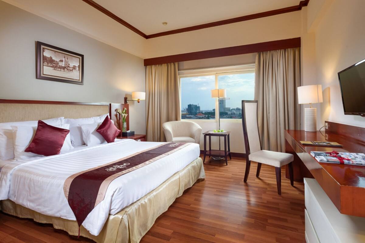 A hotel room with a large bed, a desk, a chair, and a TV.