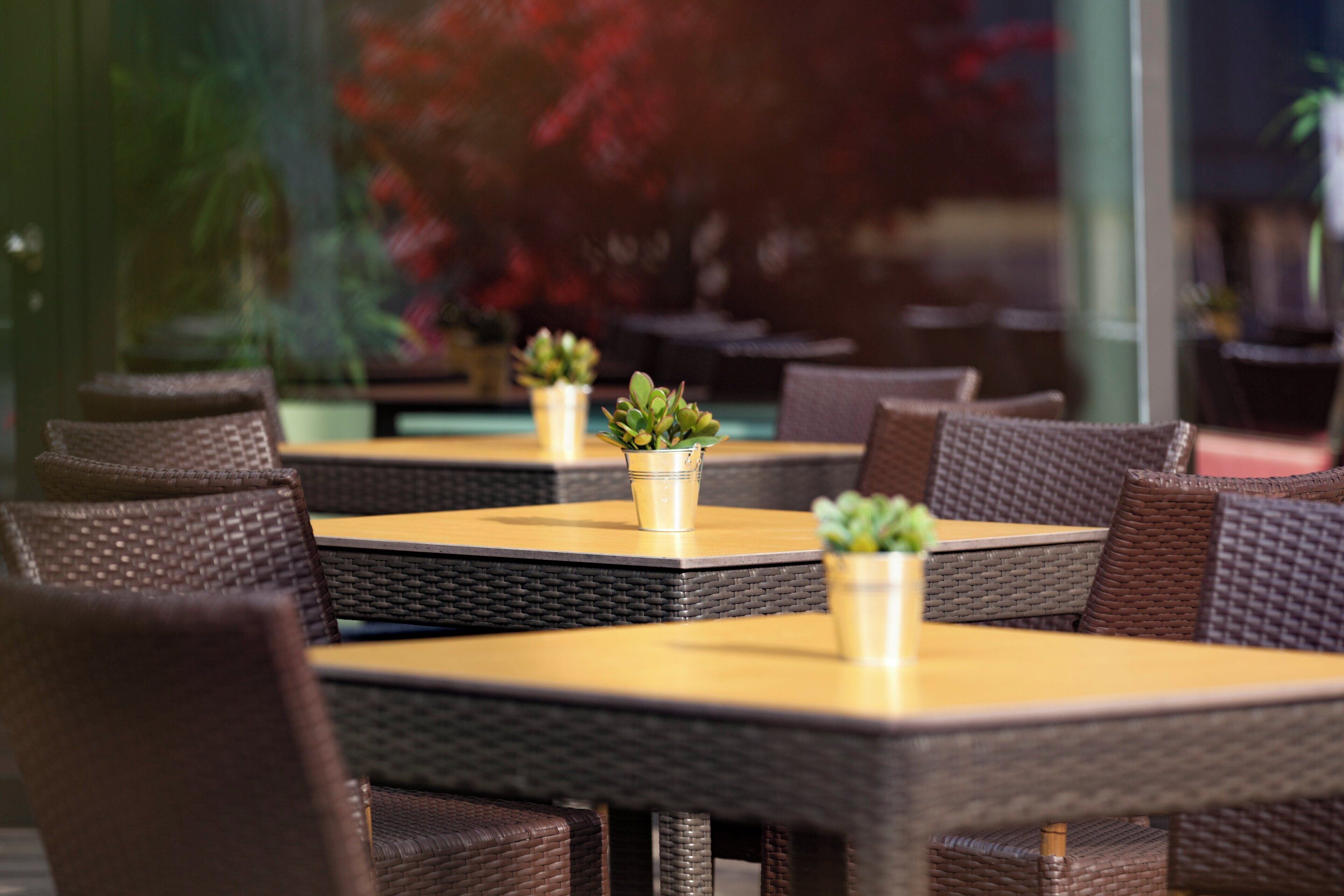 A restaurant with wicker furniture and small potted plants on the tables.