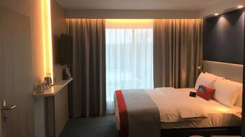 A hotel room with a bed, a bedside table, a TV, and a window with curtains.