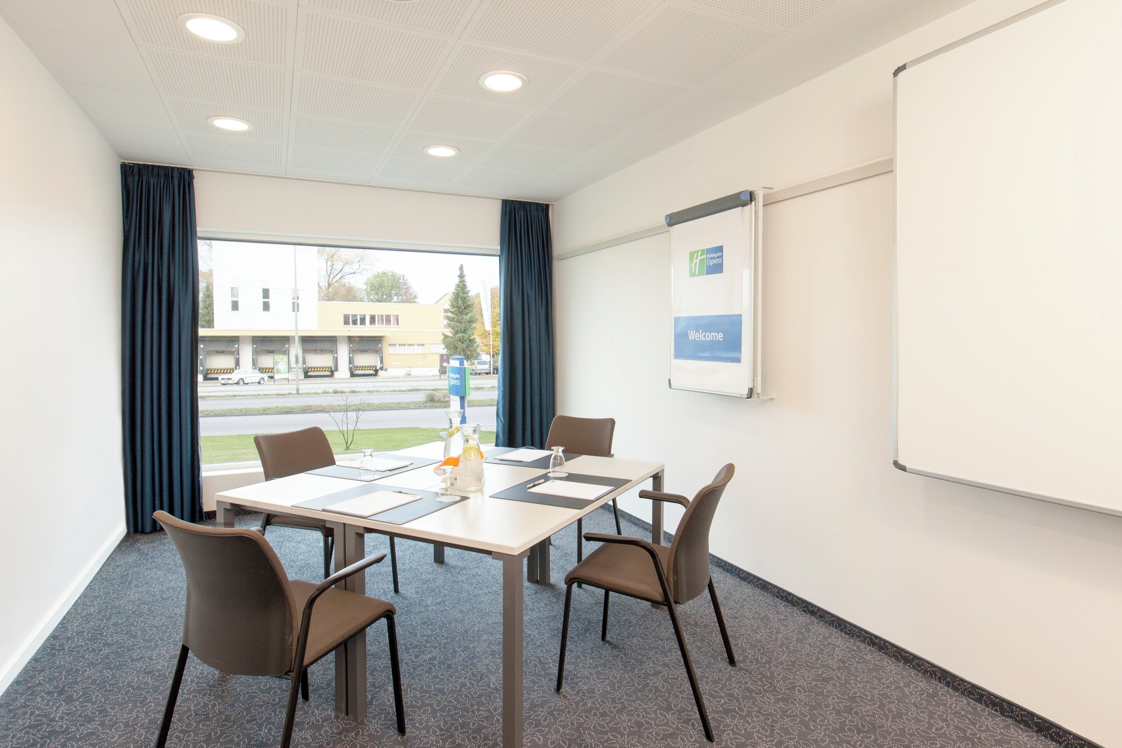 Un salón de conferencias con una mesa, sillas, una pantalla de proyector y vistas al exterior.