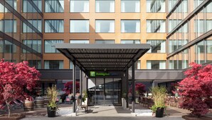 A Holiday Inn Express building with a covered entrance, potted plants, and outdoor seating. - Holiday Inn Express Zurich Airport by IHG (Ruemlang)