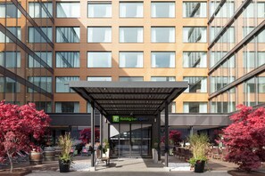 A Holiday Inn Express building with a covered entrance, potted plants, and outdoor seating. - Holiday Inn Express Zurich Airport by IHG (Ruemlang)