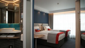 A hotel room with a large bed, a bedside table, a bathroom with a sink, and a mirror. - Holiday Inn Express Zurich Airport by IHG (Ruemlang)