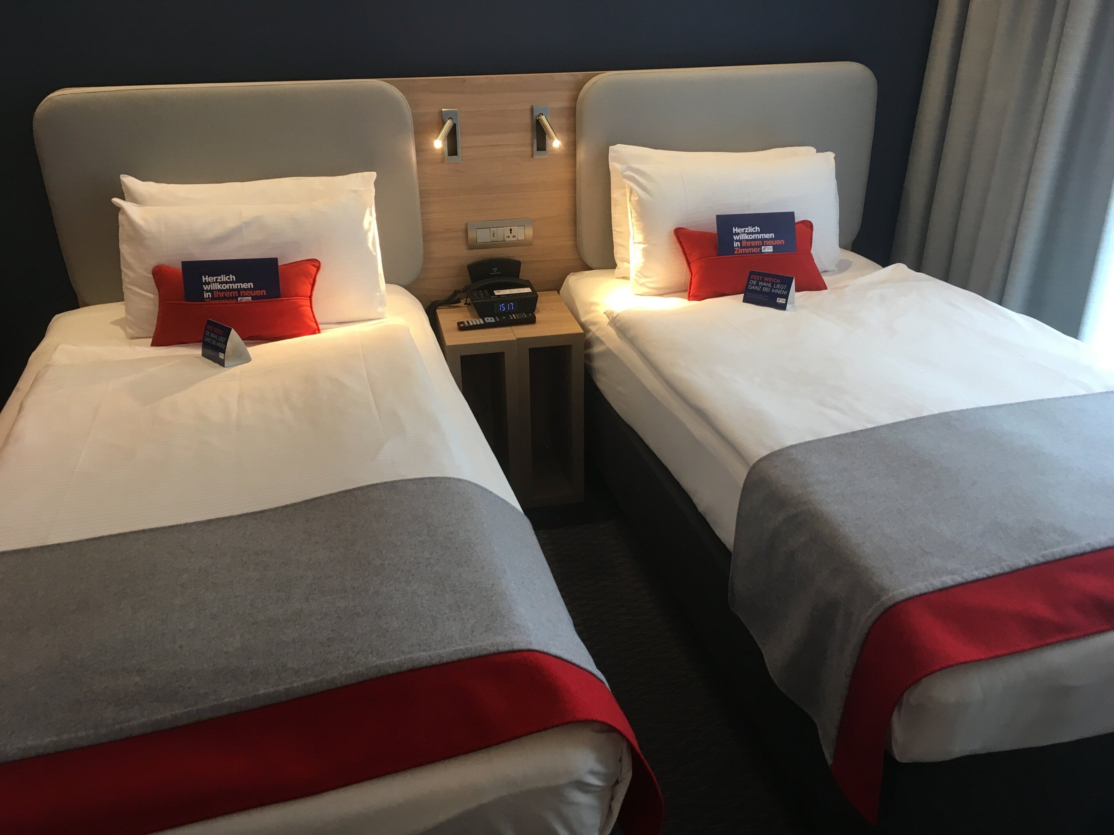 A hotel room with two beds, each with a pillow and a bedside table with a phone and a clock.