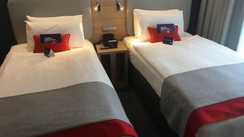 Quarto de hotel com duas camas, cada uma com travesseiro e mesa de cabeceira com telefone e relógio.