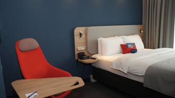A hotel room with a bed, a desk, a chair, a nightstand, and a wall-mounted phone.
