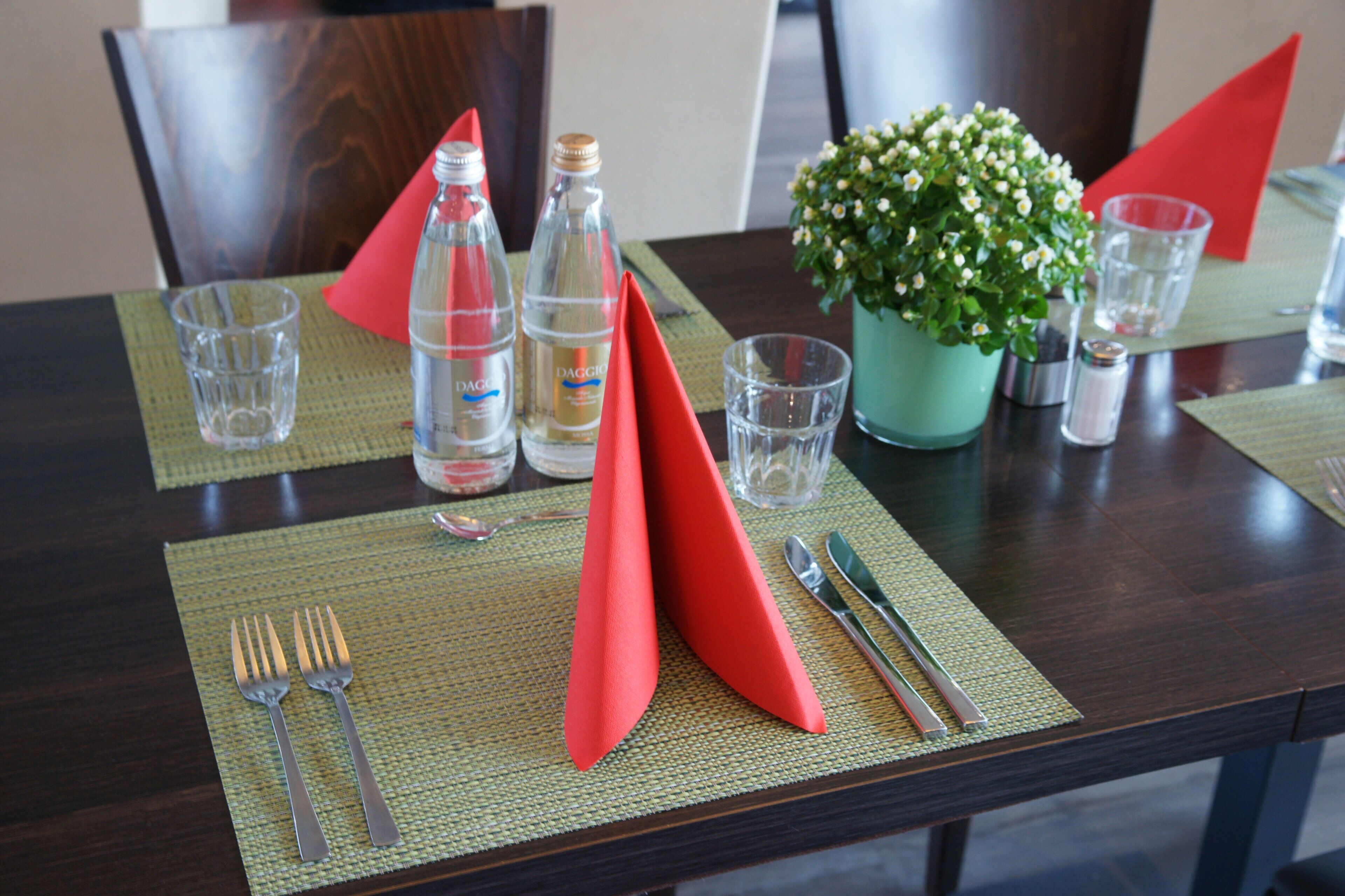Una mesa de comedor dispuesta con servilletas rojas, cubiertos y copas de cristal.