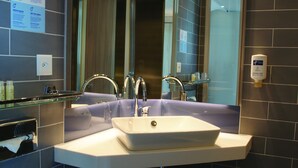 A modern bathroom with a large mirror, a white sink, and a glass shelf. - Holiday Inn Express Zurich Airport by IHG (Ruemlang)