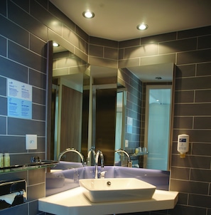 A modern bathroom with a large mirror, a white sink, and a glass shelf. - Holiday Inn Express Zurich Airport by IHG (Ruemlang)
