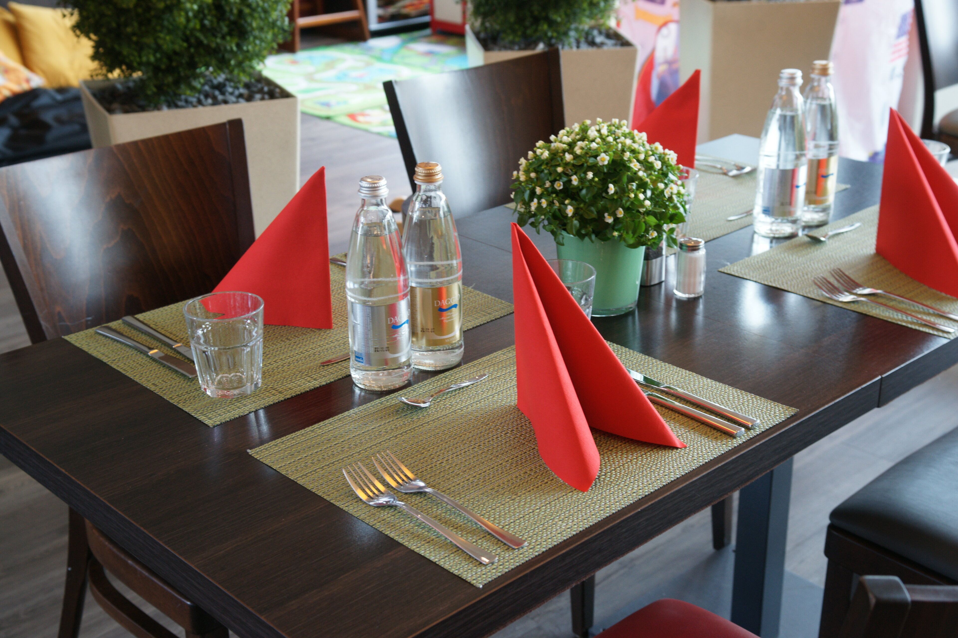 Een eettafel gedekt met rode servetten, waterflessen en een kleine potplant.