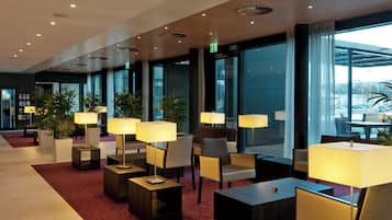 A modern hotel lobby with seating areas, tables, and large windows offering a view of the city.